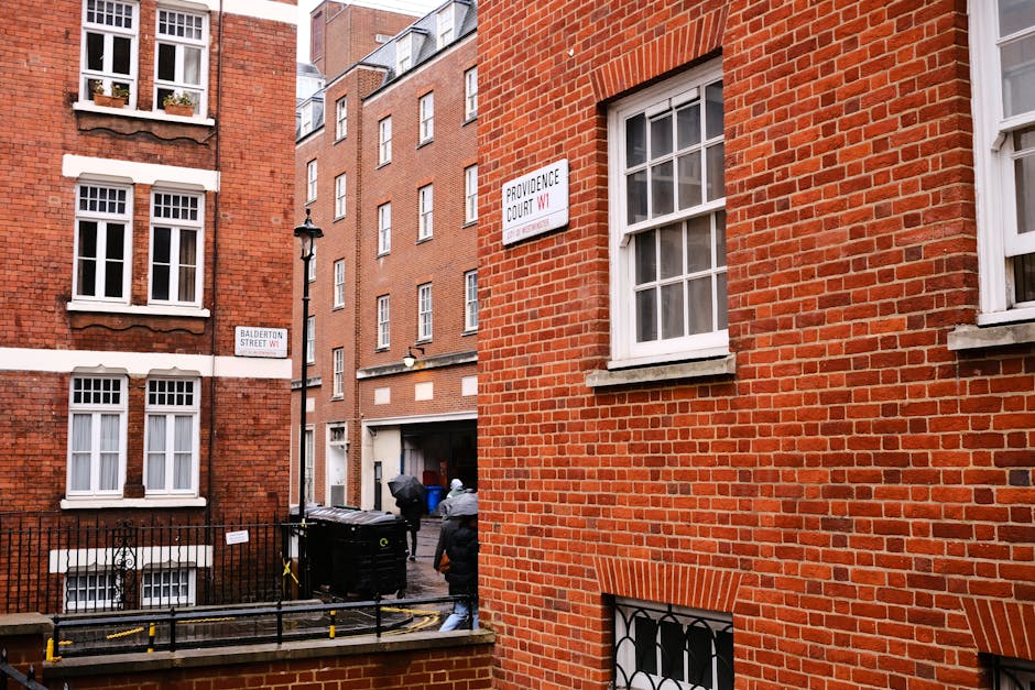 A busy Marylebone street scene during daytime featuring a row of multi-story brick buildings with commercial shops on the ground floor. The building facades include arched windows and balconies, with
